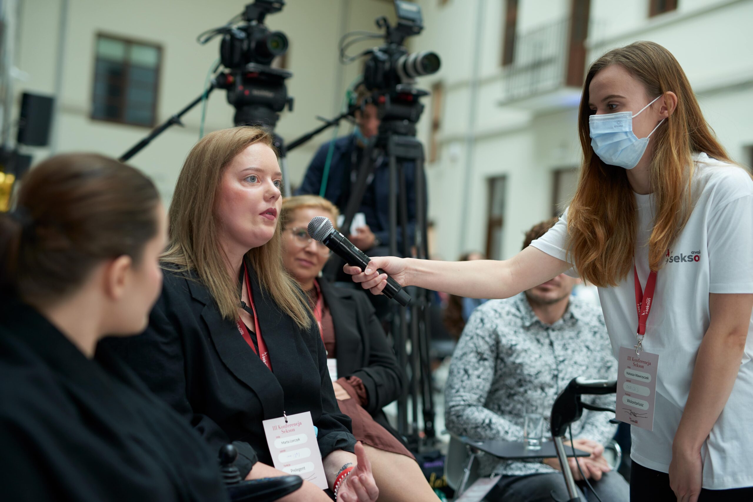 Wolontariuszka podaje mikrofon uczestnice konferencji.