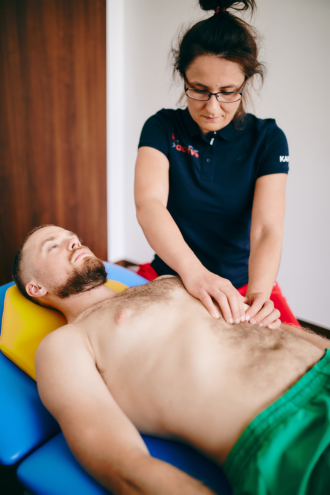 Na zdjęciu fjzoterapeutka masująca brzuch pacjenta leżącego na leżance.