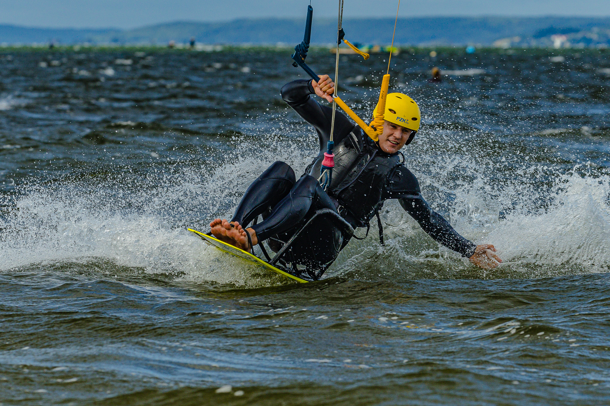 Uśmiechnięty mężczyzna płynie na siedząco na kiteboardzie.